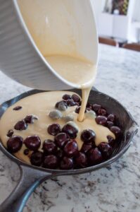 skillet filled with cherries and batter being poured over the top