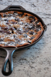 Cast iron skillet with cooked cherries and batter dusted with powdered sugar