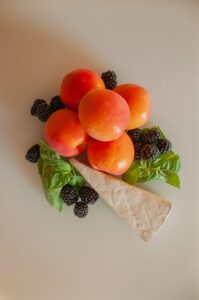 fresh whole apricots with blackberries, fresh basil and a slice of brie gathered together on flat service