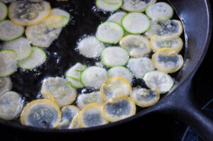 thin coins of zucchini frying in a cast iron pan with an inch of oil